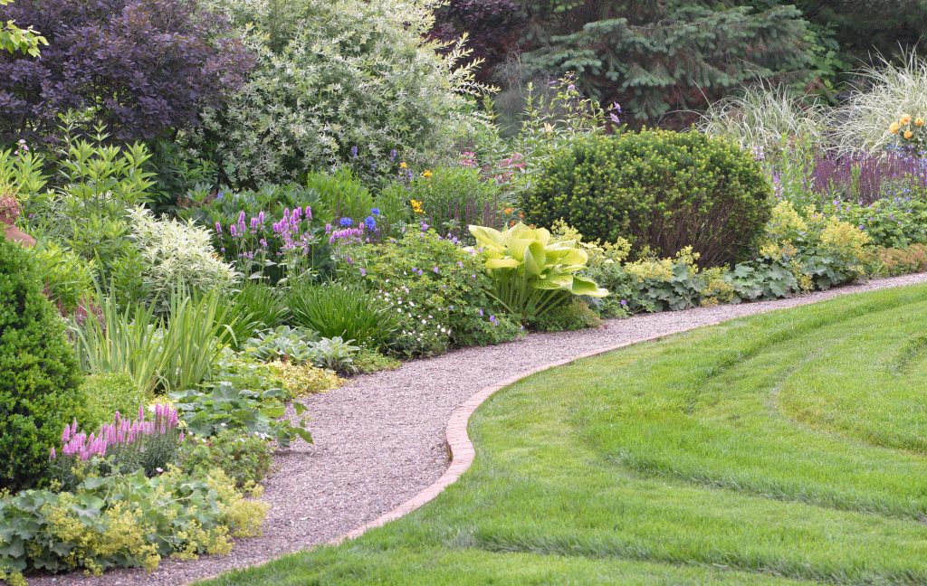 Mixed garden bed along a curved gravel path bordered by lawn