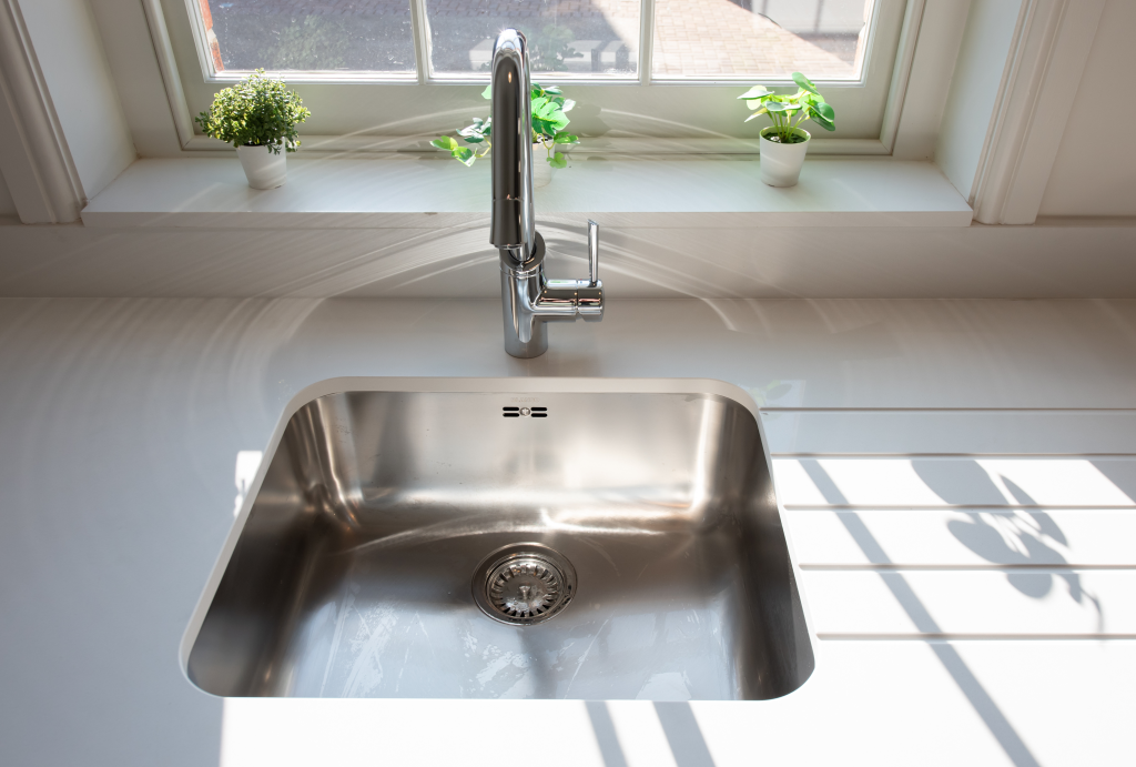 A clean kitchen sink with a faucet placed under a window with potted plants on the windowsill